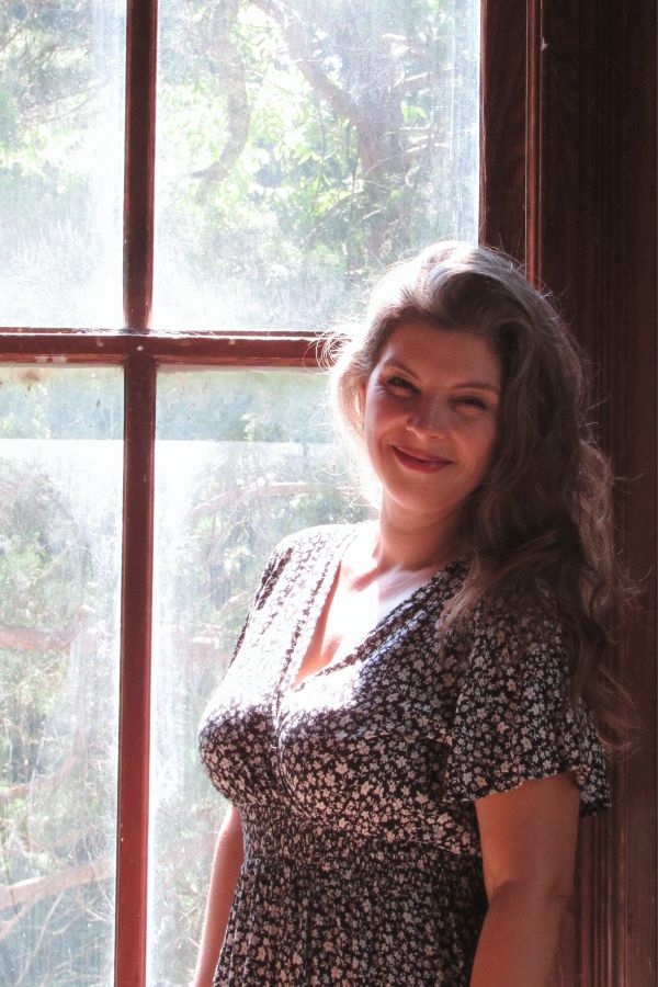 woman standing infront of the window of an old house with sun coming though the window